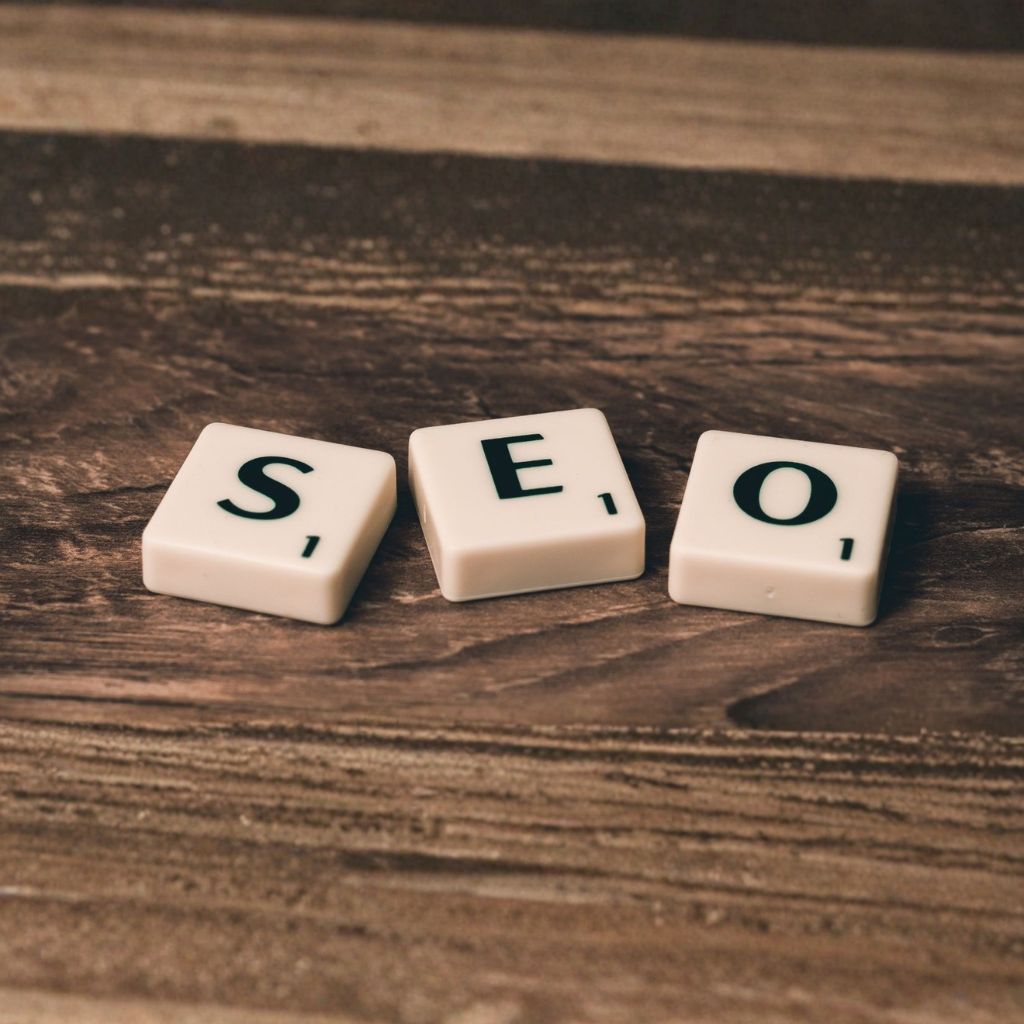 Close-up shot of three white Scrabble tiles on a dark wood grain surface spelling out the letters "SEO.