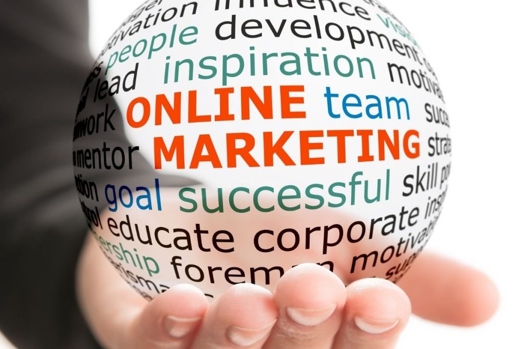 A hand holding a transparent glass orb, which contains a word cloud with words like "ONLINE MARKETING," "team," and "inspiration" highlighted in red.