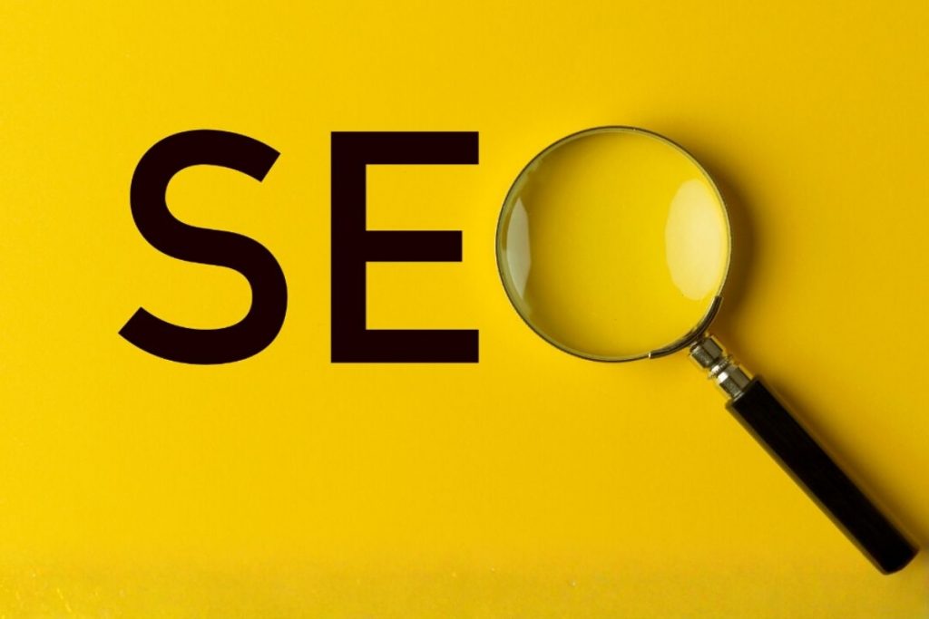 The letters "SEO" (Search Engine Optimisation) in large black text on a bright yellow background, with a magnifying glass placed over the letter 'O'.
