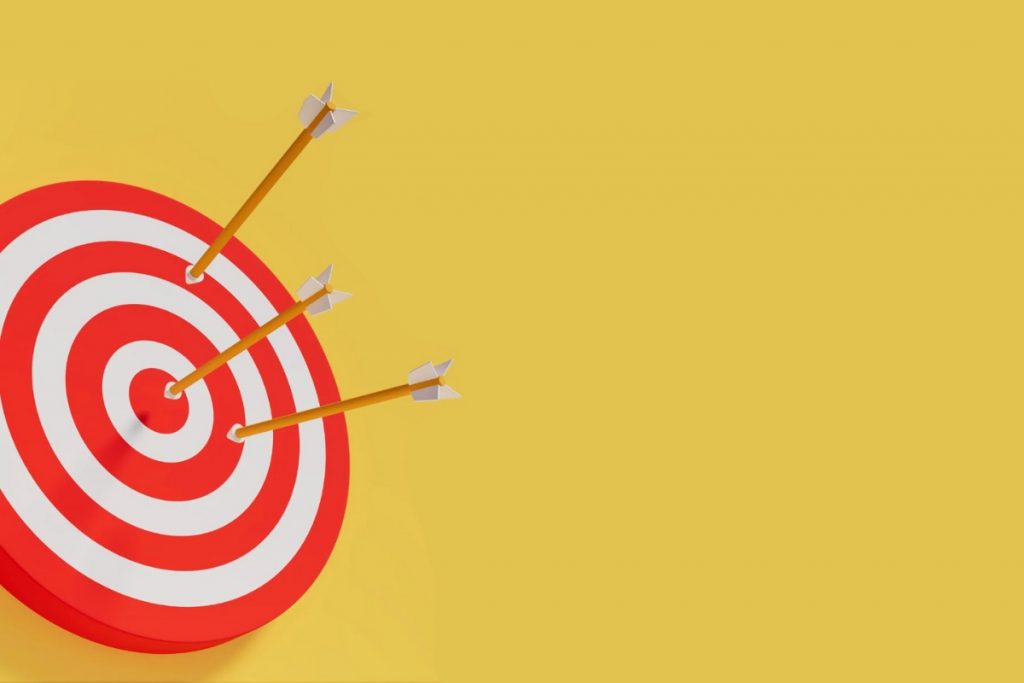 A red and white bulls-eye target on a solid yellow background, with three arrows stuck in it, one hitting the center.