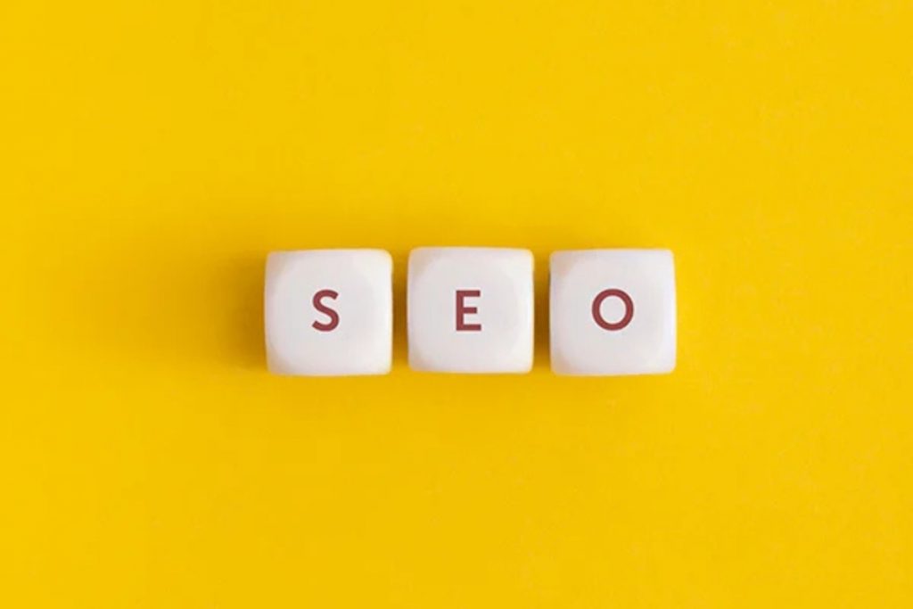 Three white cubes placed in a row against a solid yellow background, with the letters "S," "E," and "O" printed on them in red.