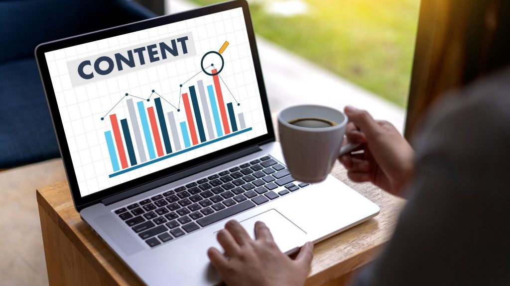 Laptop screen showing a bar chart titled 'CONTENT' with a magnifying glass. A person is holding a coffee cup.