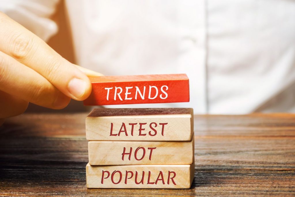 A hand places a red wooden block labeled "TRENDS" on top of a stack of three natural wooden blocks labeled "LATEST," "HOT," and "POPULAR," symbolising search trends.