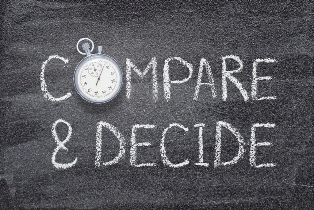 The words "COMPARE & DECIDE" written in chalk on a dark gray chalkboard texture, with a silver stopwatch replacing the 'O' in 'COMPARE'.