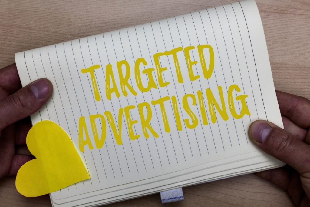 A person holding a notebook that says "TARGETED ADVERTISING" in yellow marker, with a yellow paper heart on the page.