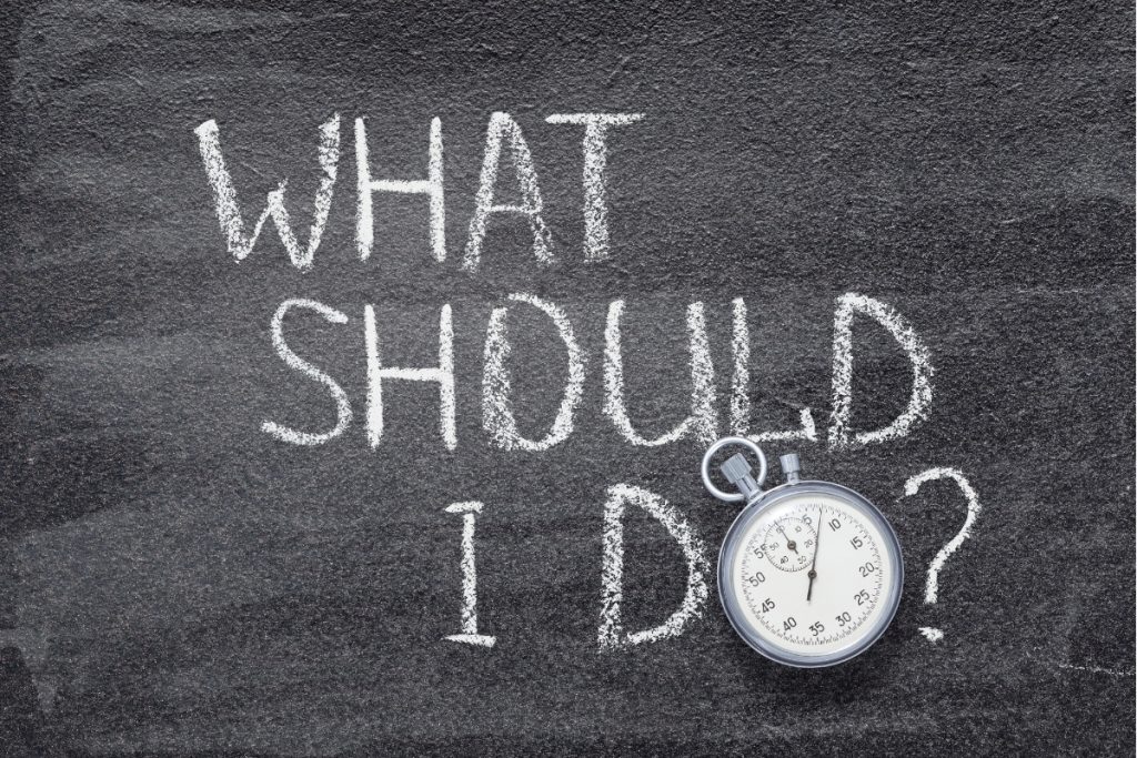 A chalkboard with the words "WHAT SHOULD I DO?" written in chalk next to a silver stopwatch.