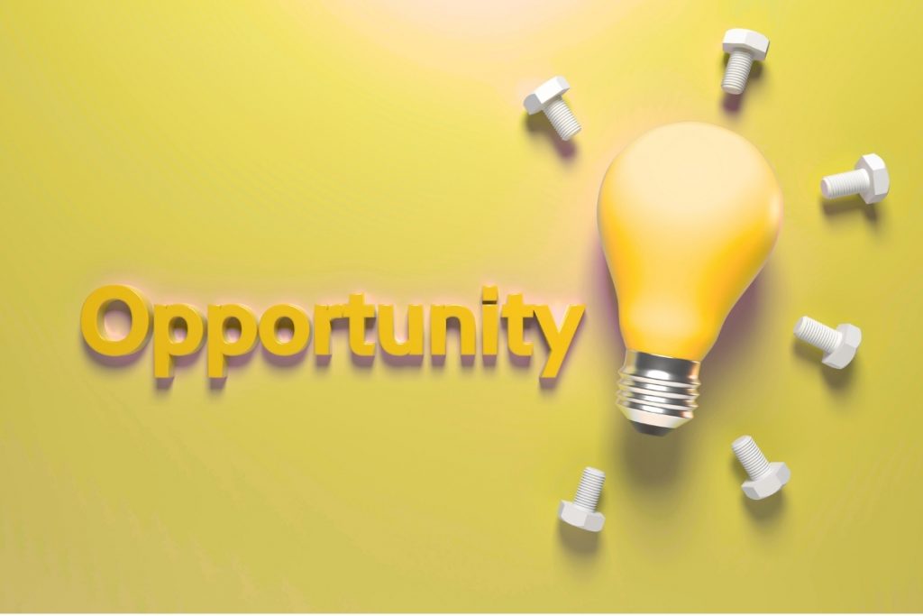 A bright yellow lightbulb surrounded by metal bolts and the word "Opportunity" in 3D text.