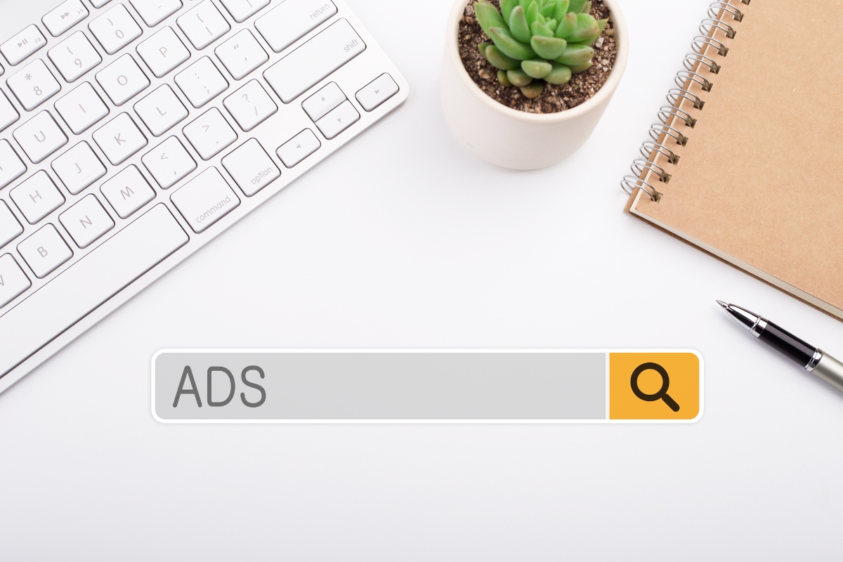 A white desk with a keyboard, a small plant, a notebook, and a search bar overlay that says "ADS."