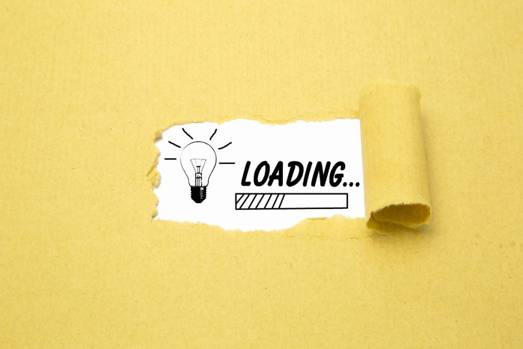 A drawing of a lightbulb and a loading progress bar visible through a torn hole in yellow paper.