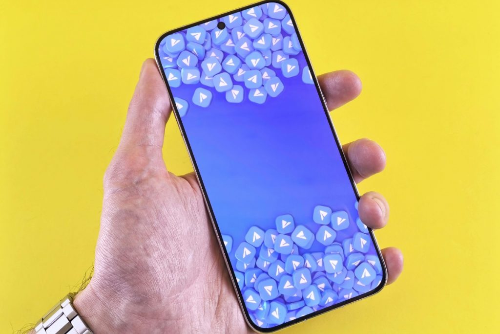 A hand holding a smartphone against a yellow background, displaying a screen filled with blue Telegram app icons.
