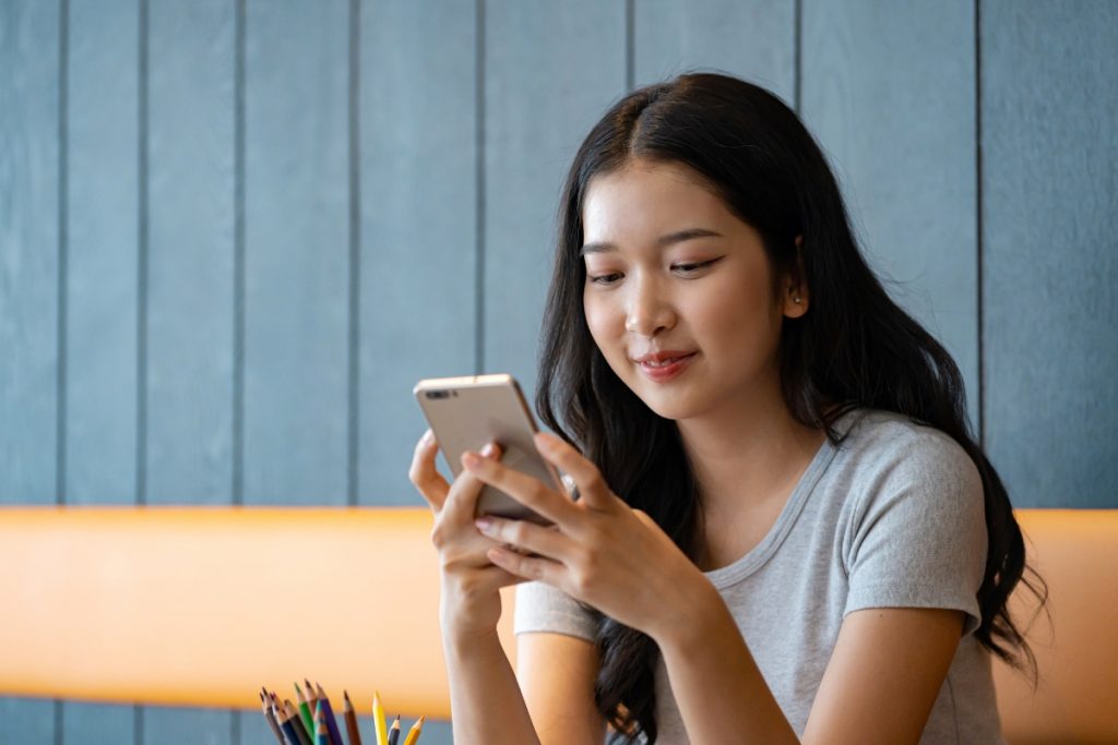 A young woman smiling while looking at and typing on her smartphone.