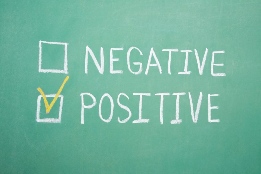 A top-down view of a person using a laptop with a smartphone and a notebook nearby, featuring a "Negative Keywords" graphic on the screen.