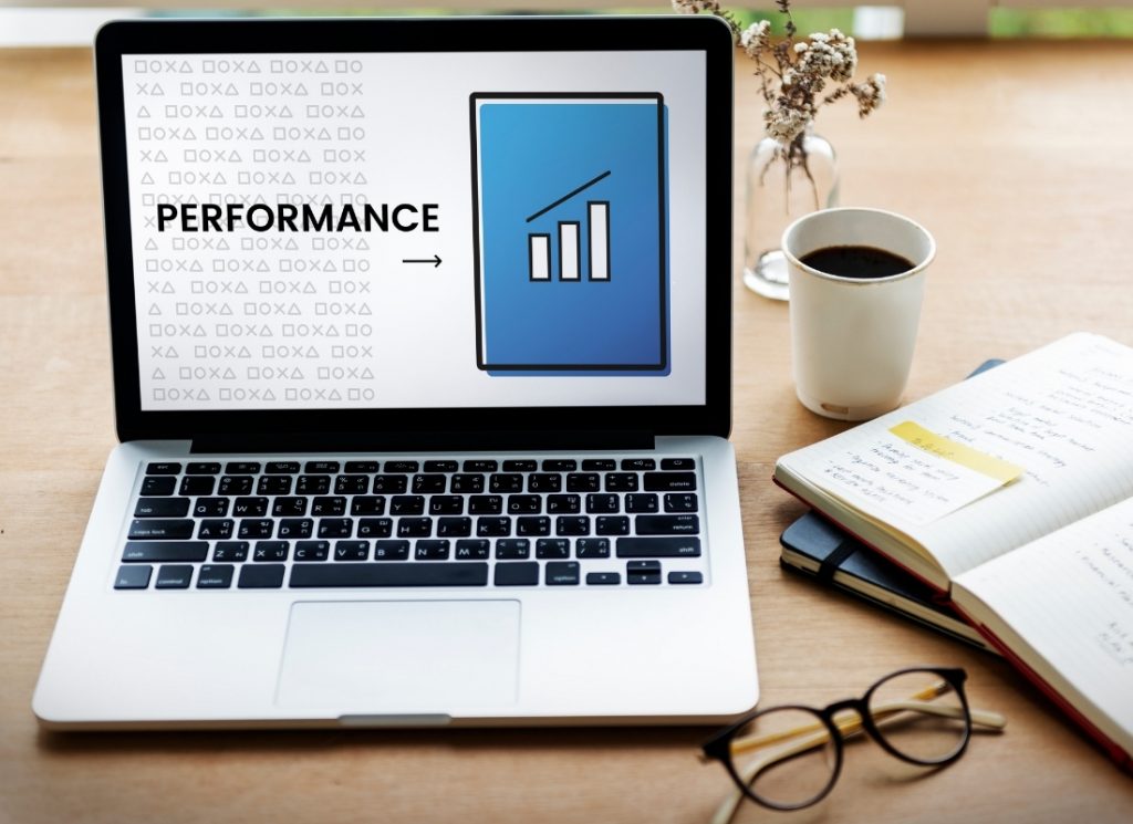Laptop on a desk displaying a "Performance" graphic with an upward-trending bar chart.