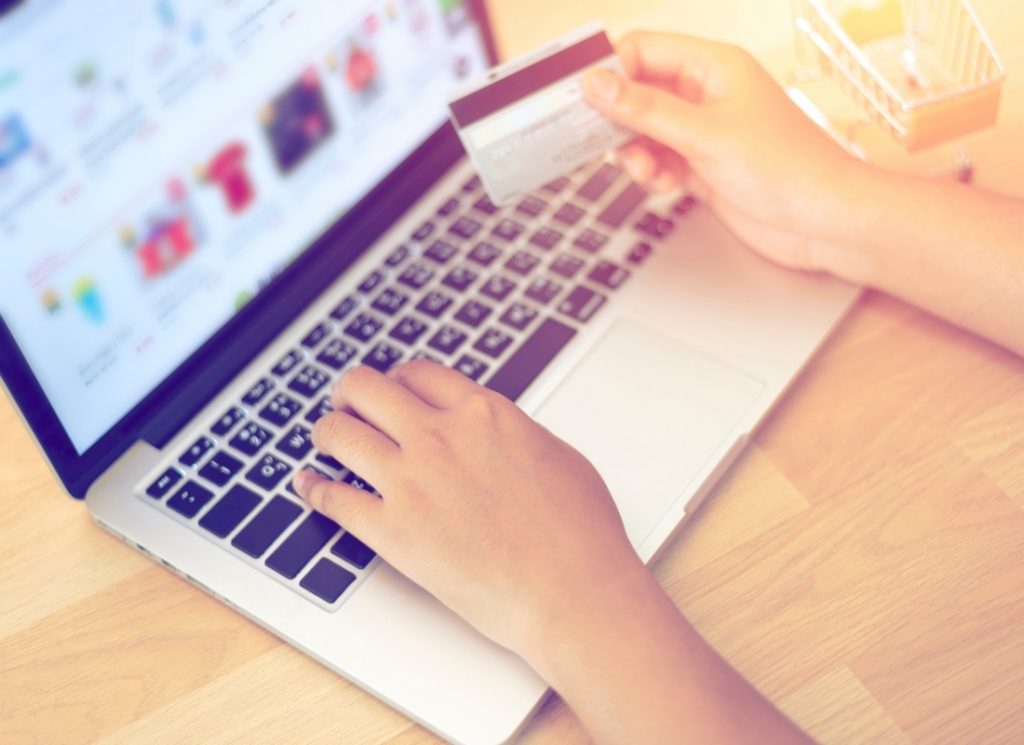 A close-up of a person holding a bank card while typing on a laptop, illustrating an online shopping transaction.