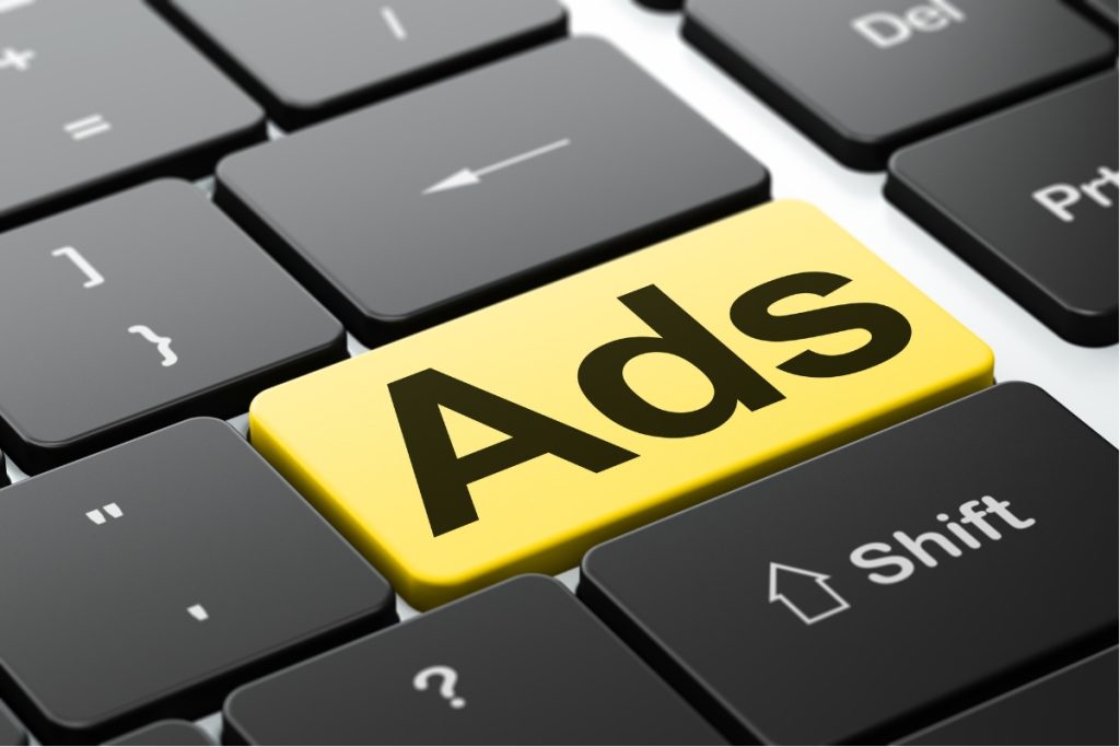 A close-up shot of a black computer keyboard featuring a prominent, bright yellow "Enter" key with the word "Ads" printed on it.