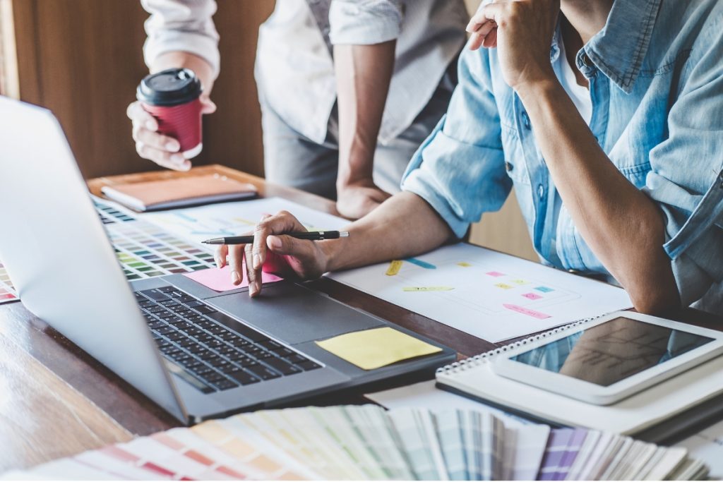 A team of professionals leaning over a table covered with wireframes, website layout sketches, and sticky notes while planning a site strategy.