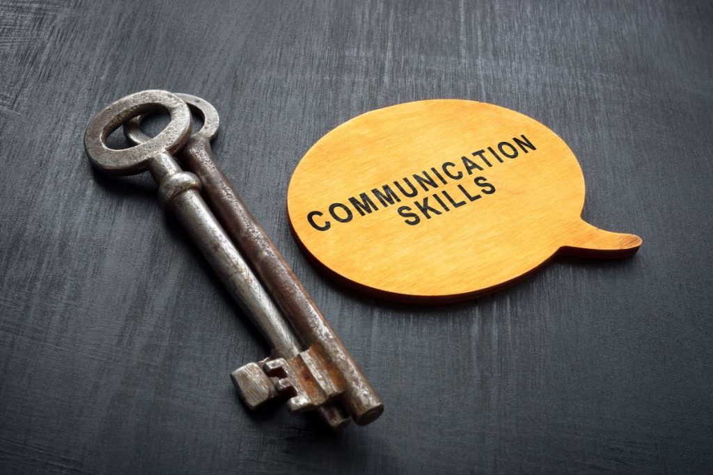 Two antique keys lying next to a yellow wooden speech bubble graphic that reads "COMMUNICATION SKILLS" on a dark wood surface.