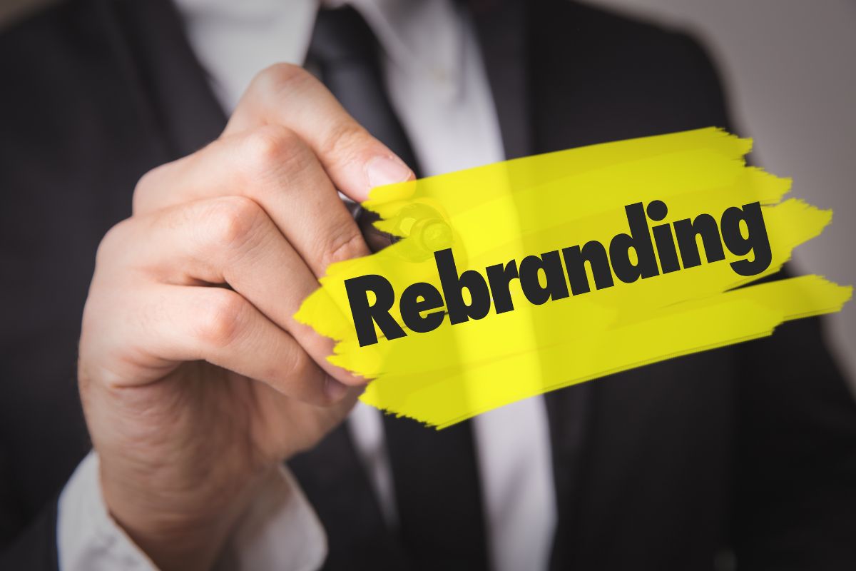 A close-up of a person in a suit holding a marker over a highlighted yellow bar featuring the word "Rebranding."